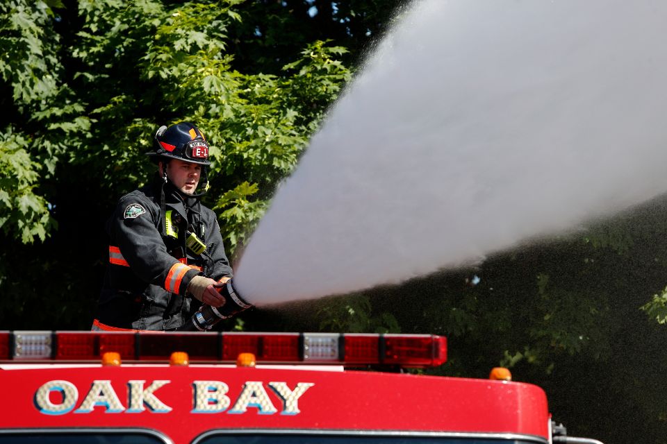 An Oak Bay Firefighter controls a firehose on top of an Oak Bay Fire Department engine.