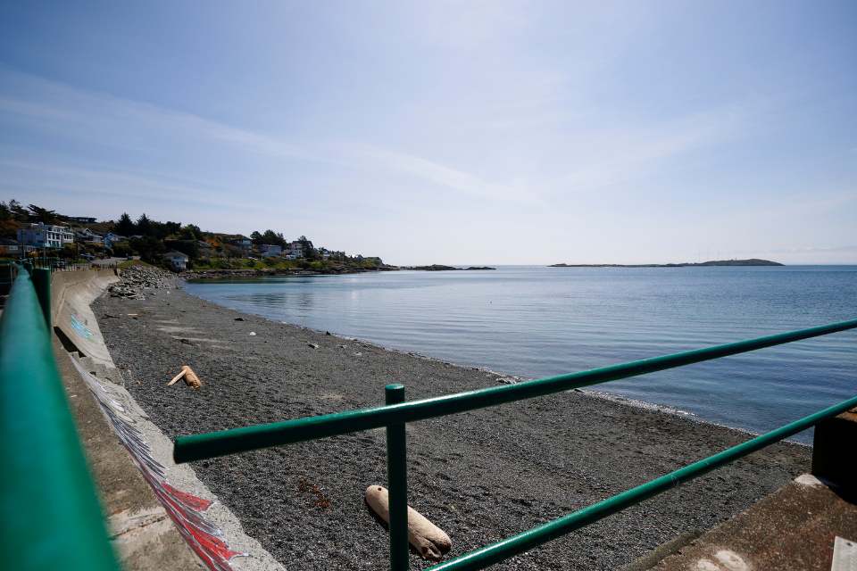 A blue sky, sunny day looking over McNeill Bay, a beach in the District of Oak Bay. The picture includes a rocky beach with the ocean stretching into the background.